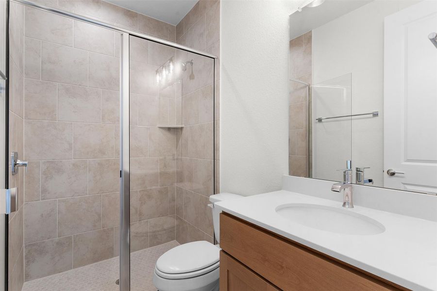 Bathroom featuring a glass-enclosed shower with tile surround, a built-in shower shelf, and a white vanity with an integrated sink and chrome faucet