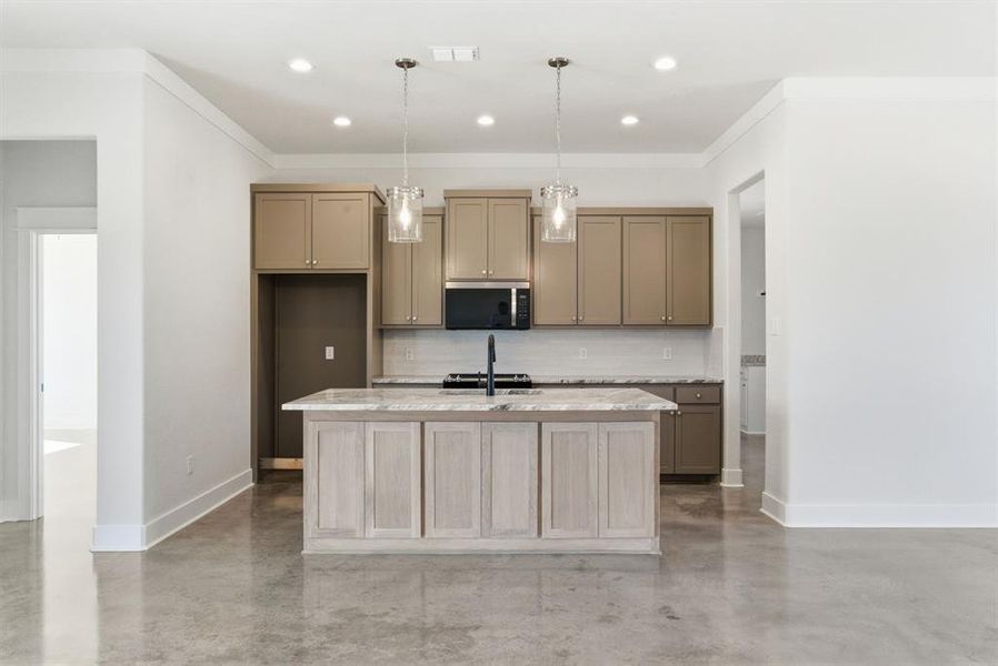 Kitchen featuring tasteful backsplash, concrete floors, hanging light fixtures, stainless steel microwave, and light stone countertops