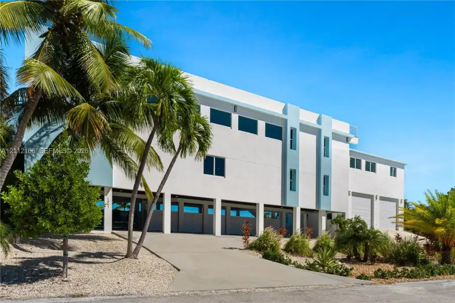 Contemporary multi-level exterior featuring white stucco finish, elevated structural design, integrated garage bays, and mature palm trees Contemporary multi-level exterior featuring white stucco finish, elevated structural design, integrated garage bays, and mature palm trees
