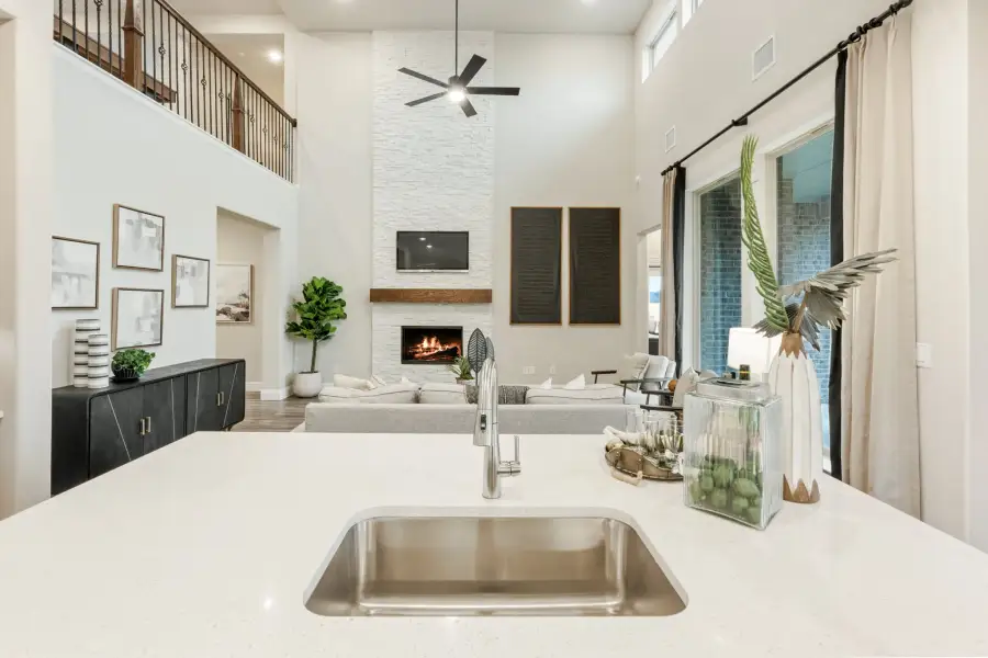 Open-concept living area viewed from kitchen island with white quartz countertop, stainless sink, and two-story fireplace wall beyond.