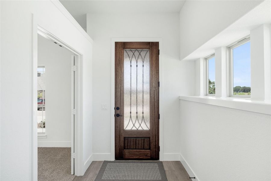 Entryway with dark wood front door featuring decorative glass panel, white walls, and hardwood floors