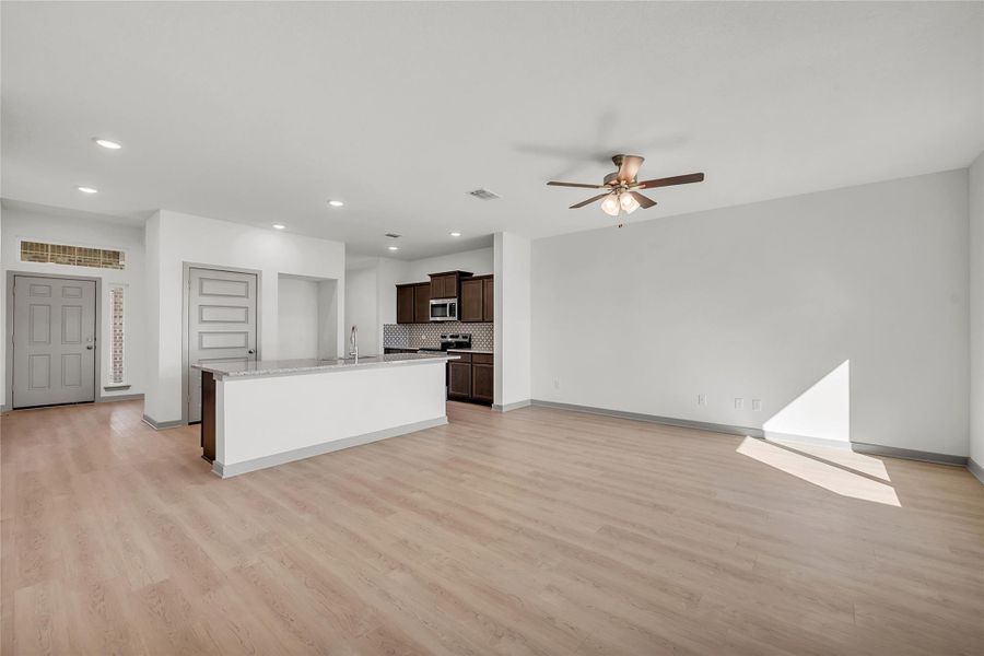Kitchen with open floor plan, dark brown cabinetry, a kitchen island with sink, light wood-type flooring, and stainless steel microwave