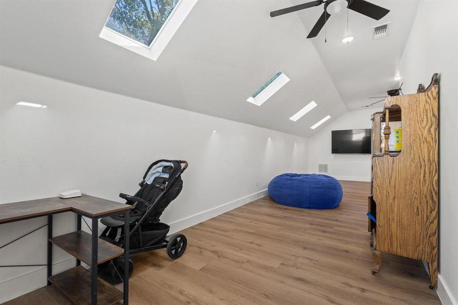 Office space with a skylight, vaulted ceiling, light wood finished floors, and ceiling fan