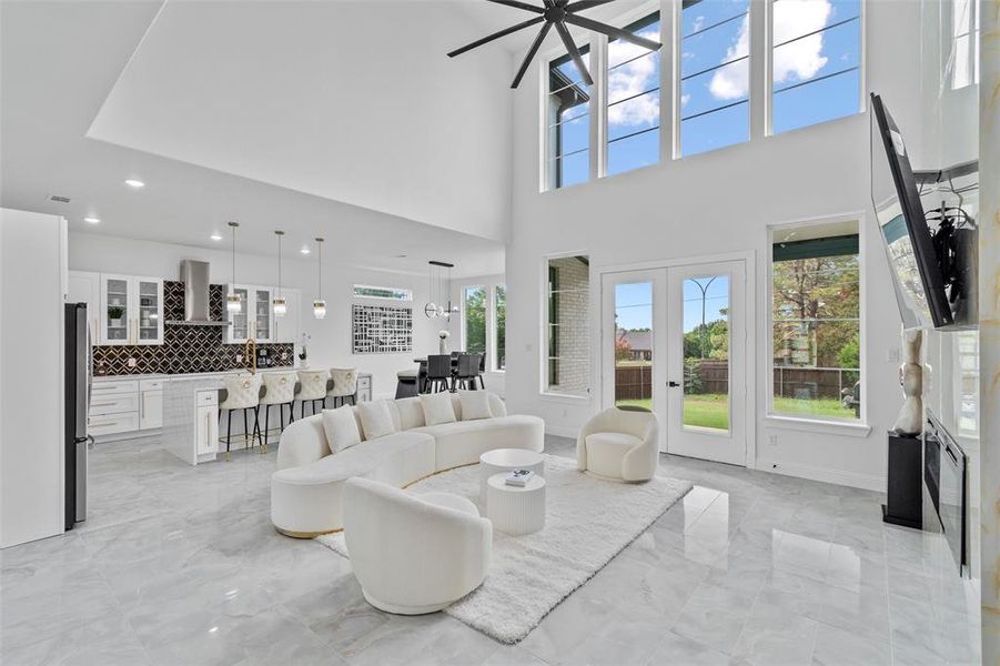 Great room featuring soaring ceilings, a full wall of transom windows, and light gray marble-finish flooring