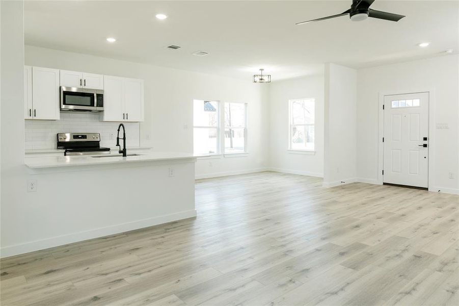 Kitchen featuring white cabinetry, stainless steel appliances, decorative backsplash, sink, and light wood-type flooring