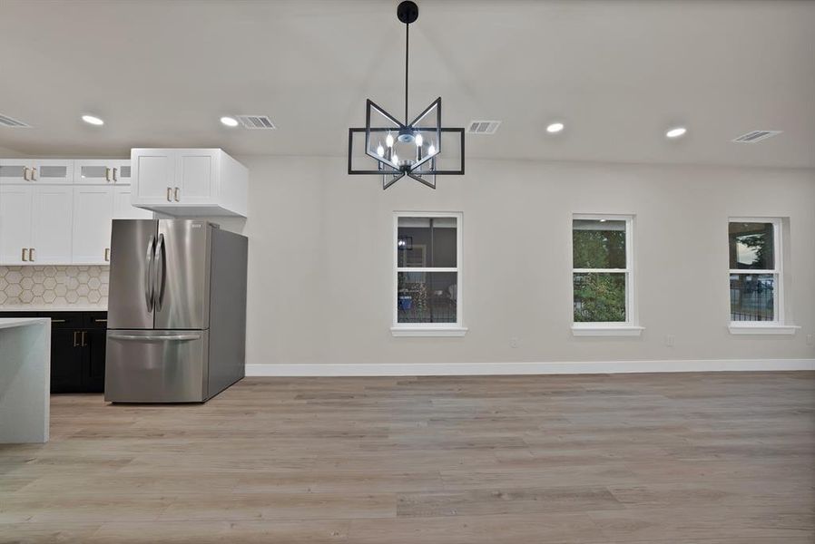 Kitchen featuring white cabinetry, glass insert cabinets, backsplash, freestanding refrigerator, and hanging light fixtures