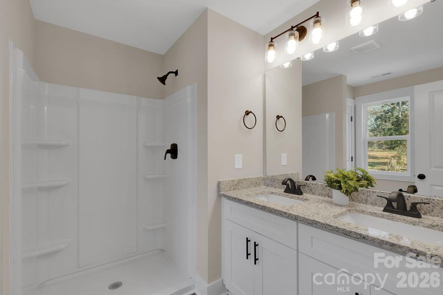 Primary bath with dual-sink vanity, granite countertops and comfort height toilet