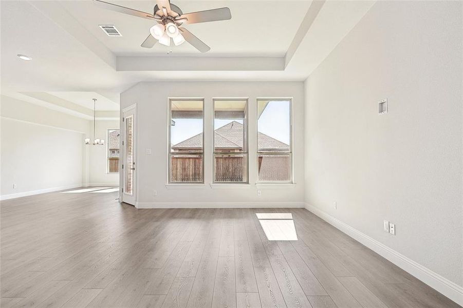 Unfurnished living room with hardwood / wood-style floors, a tray ceiling, and ceiling fan with notable chandelier