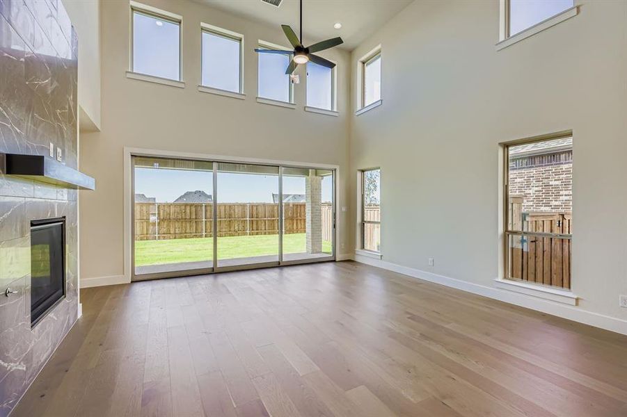 Unfurnished living room with a premium fireplace, light wood finished floors, a ceiling fan, a towering ceiling, and recessed lighting