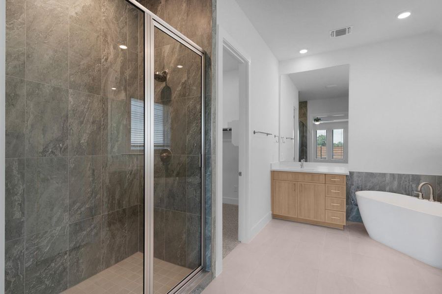 A well-lit primary bathroom features a spacious glass-enclosed shower, a modern soaking tub, and a vanity with ample storage.