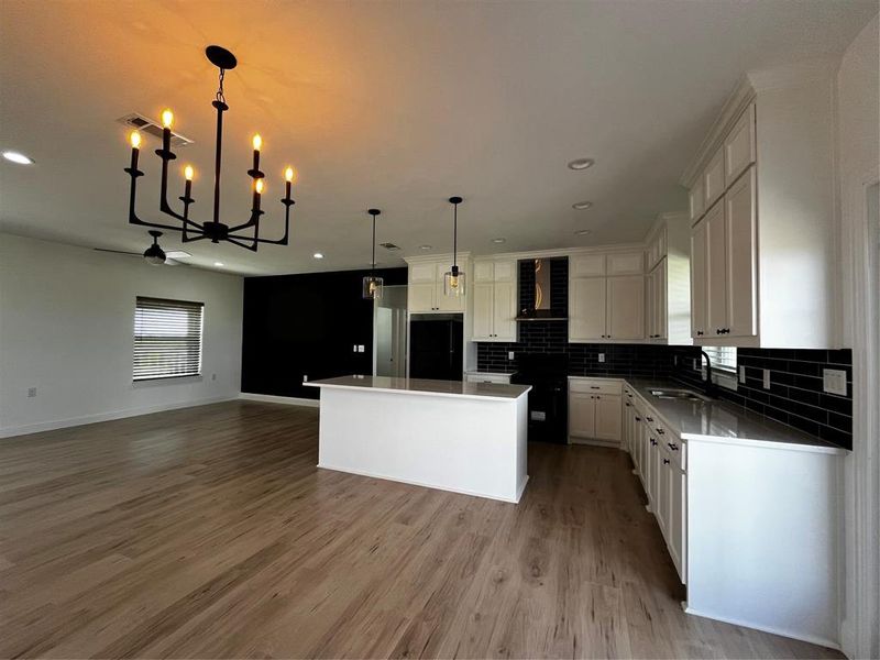 Kitchen featuring tasteful backsplash, a center island, decorative light fixtures, range hood, and light wood-type flooring Kitchen featuring tasteful backsplash, a center island, decorative light fixtures, range hood, and light wood-type flooring