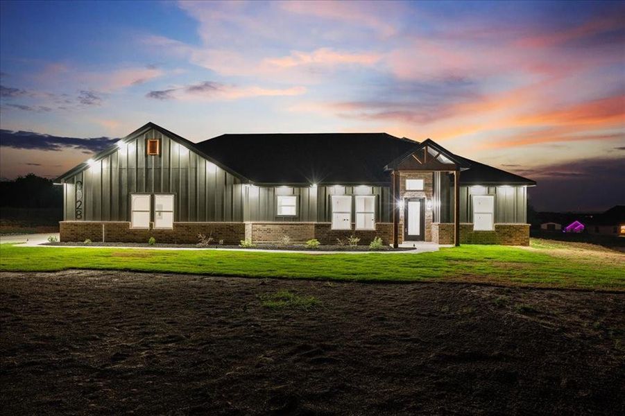 Modern farmhouse at dusk with siding, brick accents, bright exterior lighting, and great curb appeal. Modern farmhouse at dusk with siding, brick accents, bright exterior lighting, and great curb appeal.