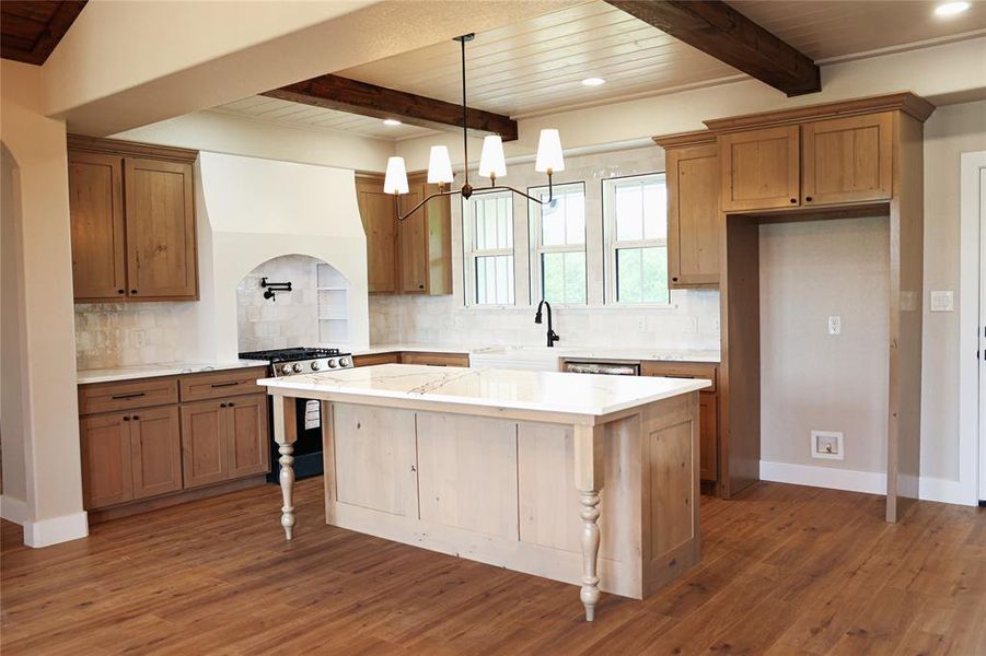Kitchen featuring wood-finish flooring, a light-toned island with decorative legs, a built-in gas range, a white tile backsplash, and light wood cabinetry