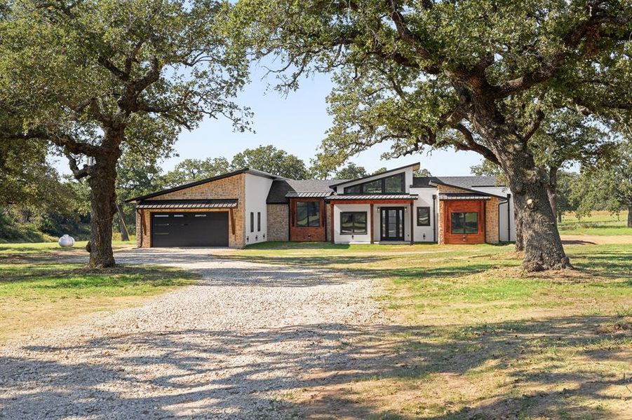 View of front of property with gravel driveway, brick siding, a front lawn, and a garage