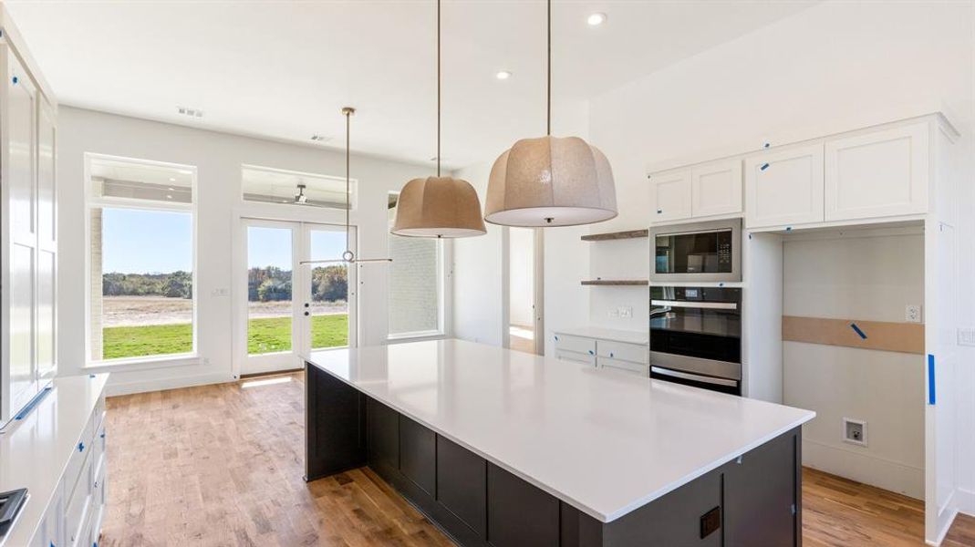 Kitchen featuring built in microwave, white cabinetry, oven, pendant lighting, and a kitchen island