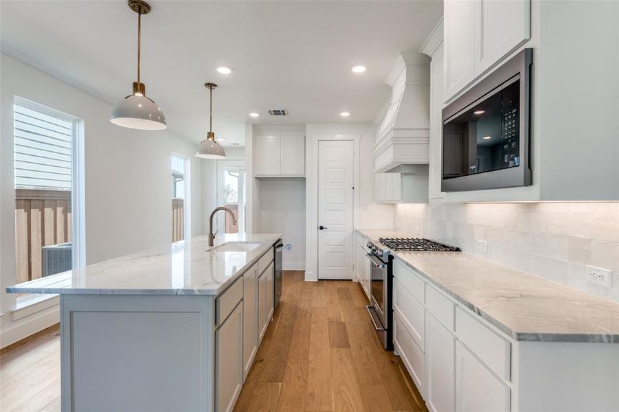 Kitchen featuring appliances with stainless steel finishes, light hardwood / wood-style flooring, tasteful backsplash, sink, and a center island with sink