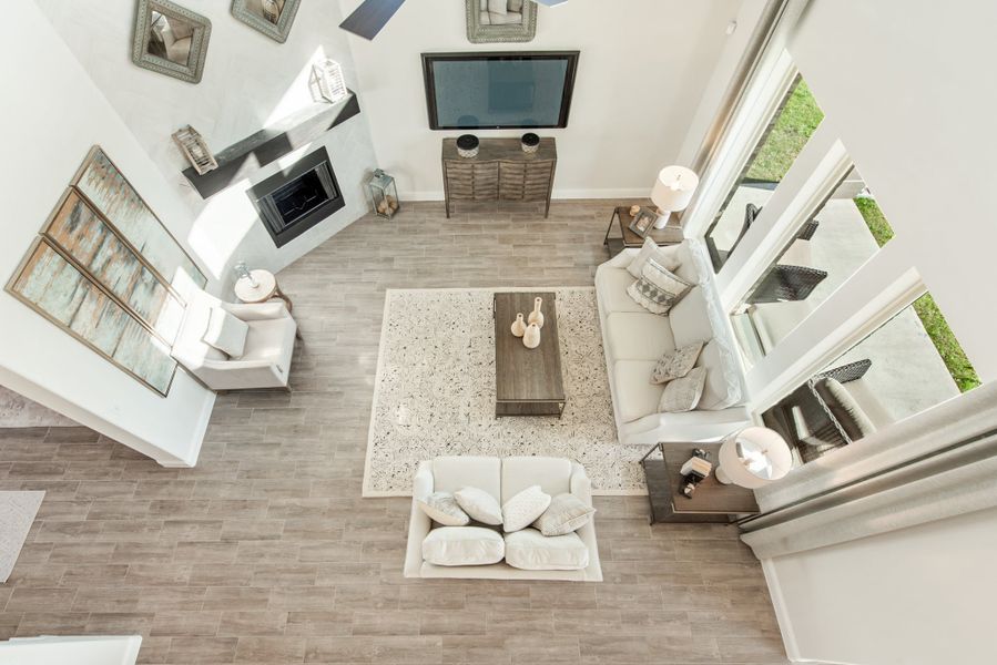 Overhead view of living room with white sofas, fireplace, wall-mounted TV, and wood-look tile floors