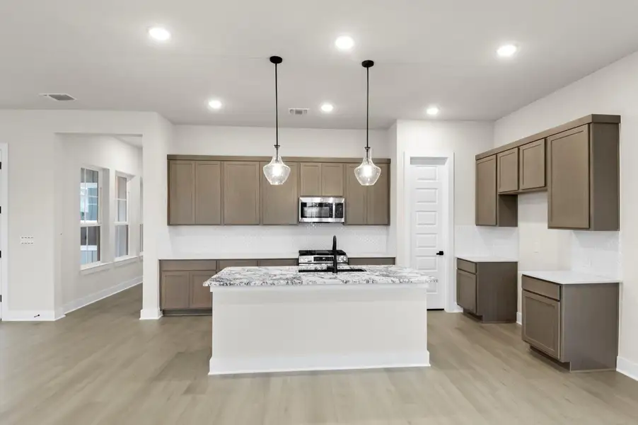 Kitchen featuring pendant lighting, light stone countertops, a kitchen island with sink, appliances with stainless steel finishes, and light wood-type flooring