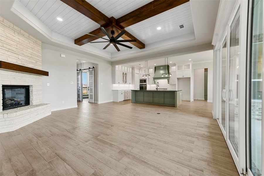 Unfurnished living room with a stone fireplace, sink, light hardwood / wood-style flooring, a barn door, and beam ceiling