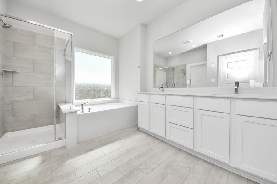 Escape to a spa-like oasis in this primary bathroom. Enjoy a walk-in shower with tile surround, a separate garden tub with custom detailing, and an elegant vanity featuring light countertops, modern hardware, and beautiful vanity lights. Experience luxury and relaxation in every detail. Sample photo of completed home with similar floor plan. Actual colors and selections may vary.