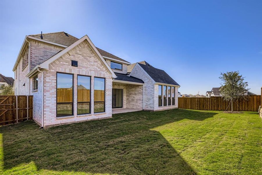Rear view of house with brick siding, a fenced backyard, a shingled roof, and a patio area