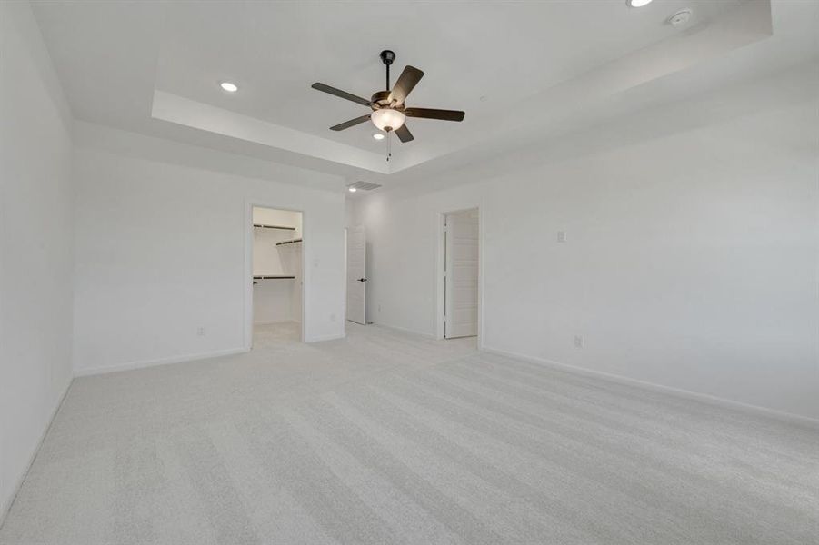 Spacious room featuring light-toned carpet, a tray ceiling with recessed lighting, and a dark-finished ceiling fan Spacious room featuring light-toned carpet, a tray ceiling with recessed lighting, and a dark-finished ceiling fan