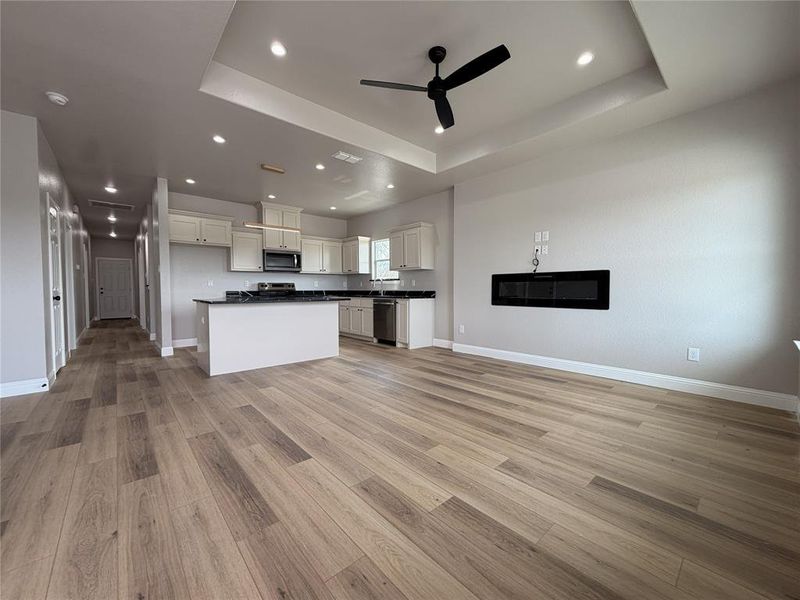 Kitchen featuring open floor plan, a kitchen island, white cabinets, a ceiling fan, and dark countertops