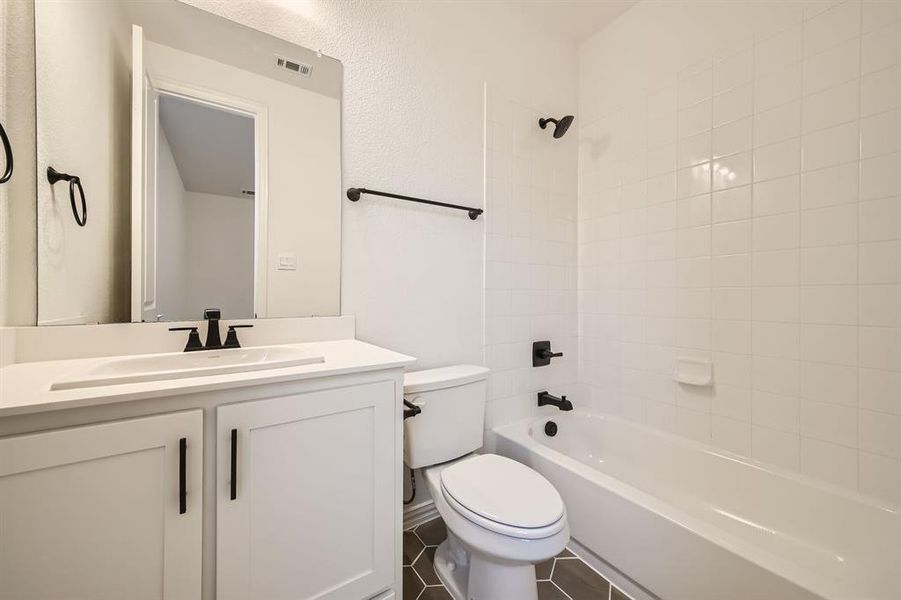 Full bathroom featuring toilet, tiled shower / bath combo, vanity, and tile patterned flooring