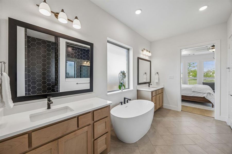 Ensuite bathroom featuring two vanities, a freestanding tub, tiled shower, light tile patterned floors, and a ceiling fan