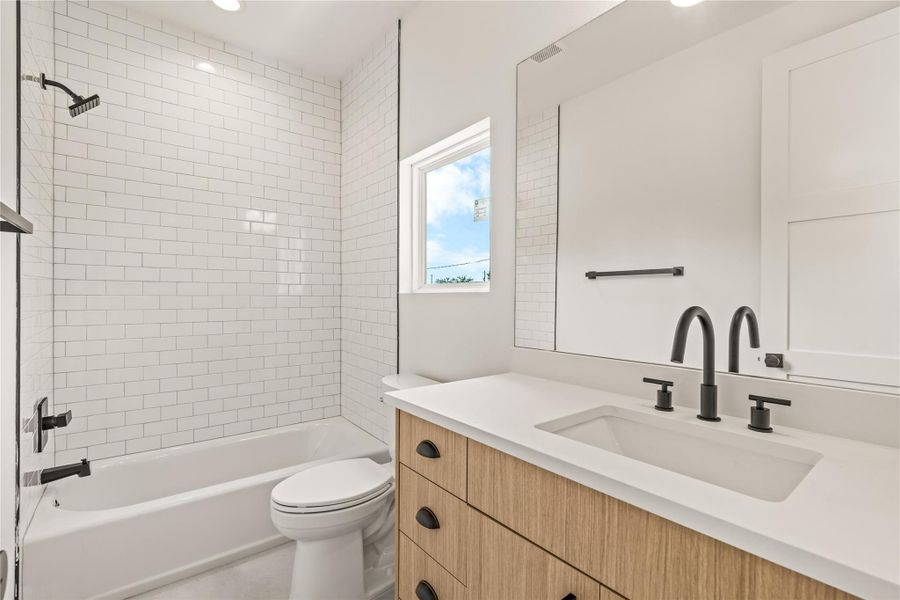 Modern guest bathroom featuring a light wood vanity with a white countertop, matte black hardware, a large frameless mirror, and a classic white subway-tiled tub/shower combination. Modern guest bathroom featuring a light wood vanity with a white countertop, matte black hardware, a large frameless mirror, and a classic white subway-tiled tub/shower combination.