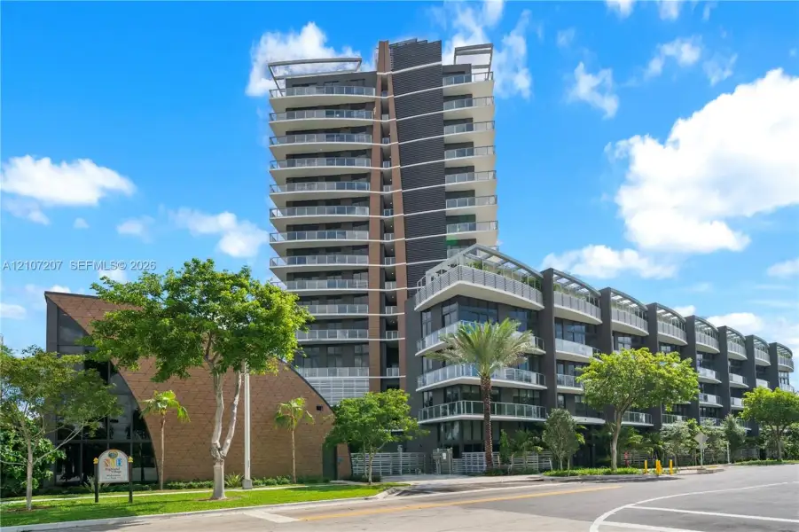 Contemporary high-rise architecture featuring glass-railed private balconies, a multi-story facade with dark paneling, and an attached low-rise structure with textured shingle-style exterior cladding Contemporary high-rise architecture featuring glass-railed private balconies, a multi-story facade with dark paneling, and an attached low-rise structure with textured shingle-style exterior cladding