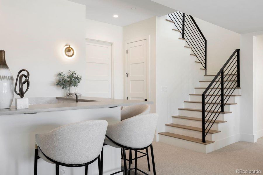 A striking staircase with sleek iron railings and light wood treads leads down to the inviting lower level, where a stylish wet bar and open entertaining spaces await.