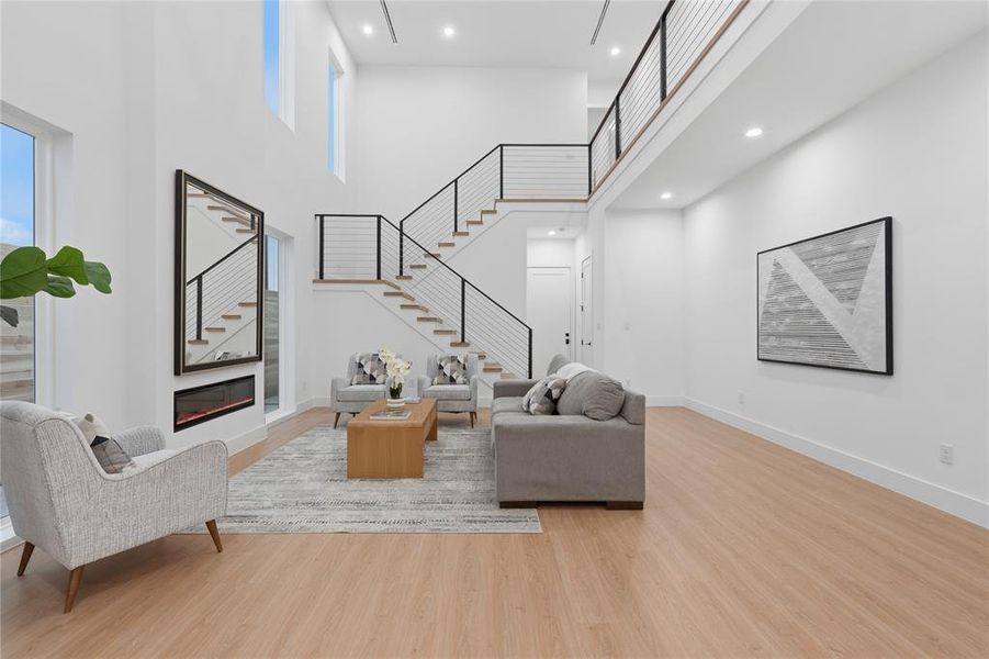 Living area featuring light wood-style floors, a high ceiling, recessed lighting, and a glass covered fireplace