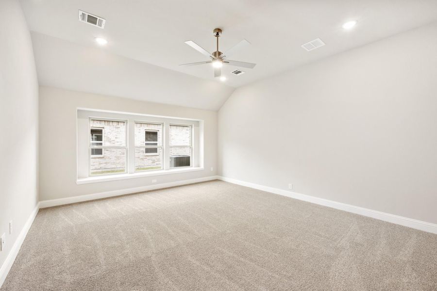Empty bedroom with vaulted ceiling, ceiling fan, carpet flooring, and triple window