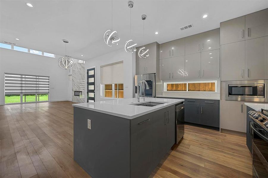 Kitchen with pendant lighting, an island with sink, sink, gray cabinetry, and stainless steel appliances