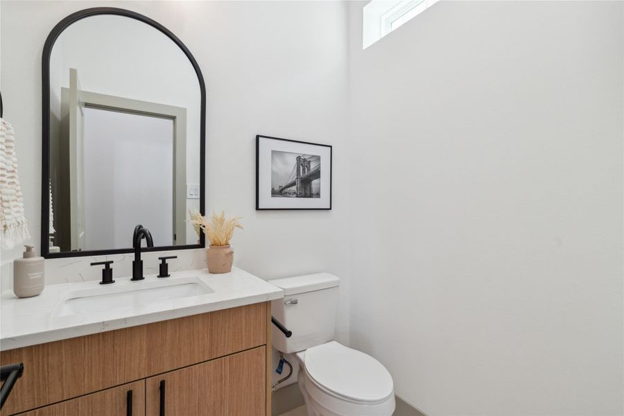 The arched mirror and matte black accents add sculptural contrast to the clean, gallery-white walls.