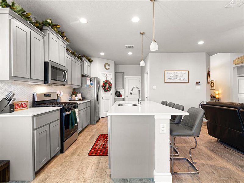 Kitchen with sink, light hardwood / wood-style flooring, pendant lighting, a breakfast bar area, and appliances with stainless steel finishes