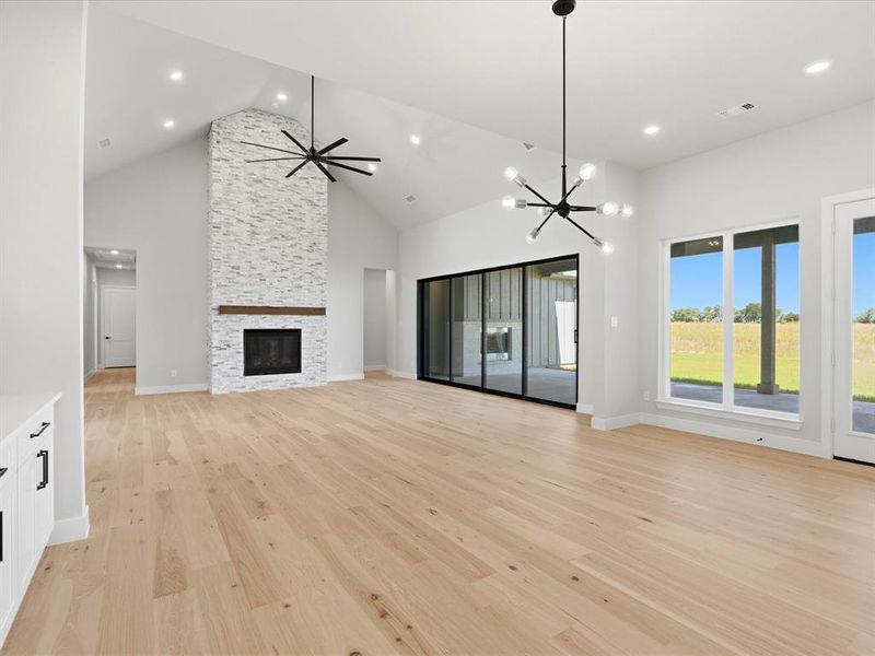 Spacious living area featuring vaulted ceilings, a floor-to-ceiling stone fireplace with a wood mantle, and light wood-finish flooring