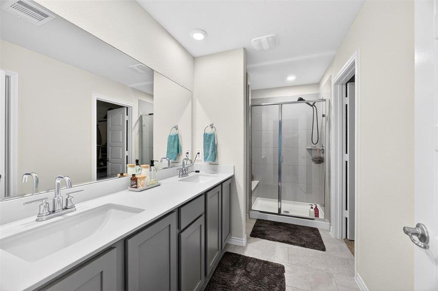 Bathroom featuring a stall shower, double vanity, light tile patterned floors, a walk in closet, and recessed lighting