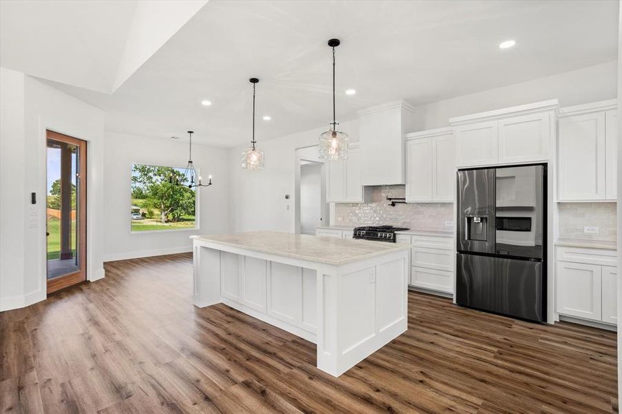 Kitchen featuring appliances with stainless steel finishes, backsplash, white cabinetry, a kitchen island, and hanging light fixtures Kitchen featuring appliances with stainless steel finishes, backsplash, white cabinetry, a kitchen island, and hanging light fixtures