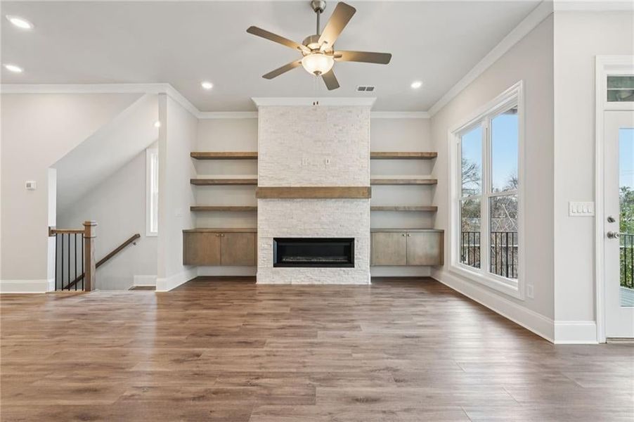 Unfurnished living room with wood finished floors, ceiling fan, a stone fireplace, ornamental molding, and recessed lighting