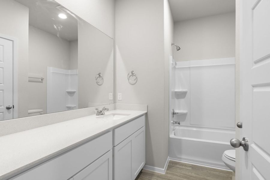 Image of a bathroom with a white dual vanity and cabinets, a large mirror, and a white shower ILO tub