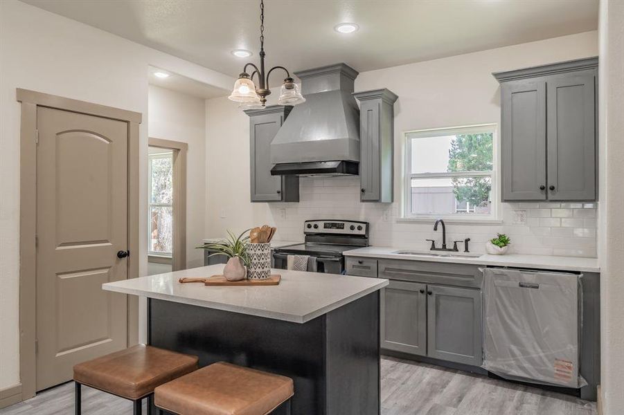 Kitchen featuring custom range hood, a breakfast bar, stainless steel appliances, backsplash, and decorative light fixtures