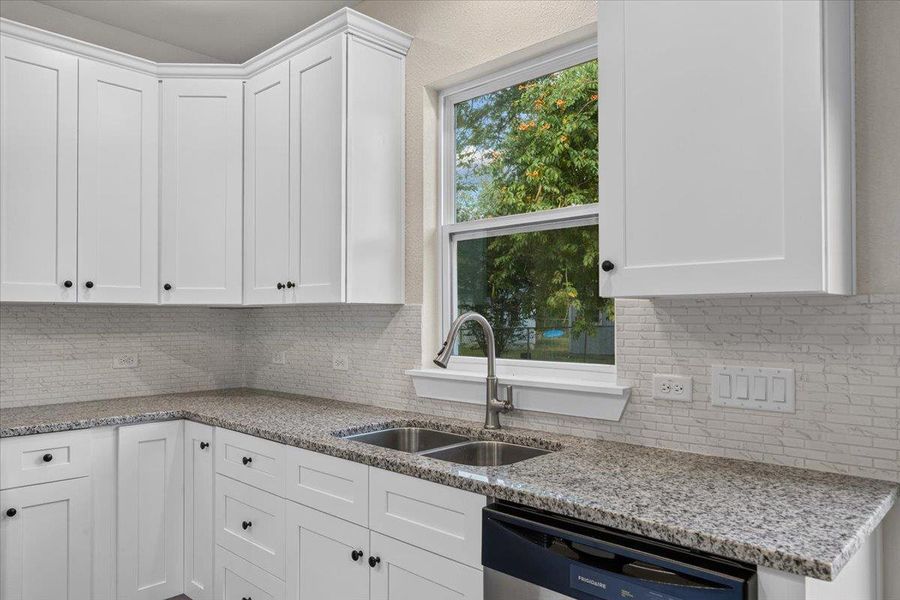 Crisp white cabinetry pairs with granite countertops under natural light from a central window. Crisp white cabinetry pairs with granite countertops under natural light from a central window.