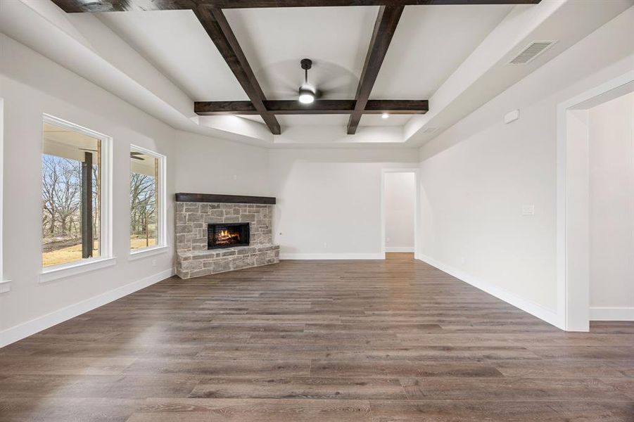 Unfurnished living room featuring coffered ceiling, ceiling fan, a stone fireplace, and dark wood finished floors Unfurnished living room featuring coffered ceiling, ceiling fan, a stone fireplace, and dark wood finished floors