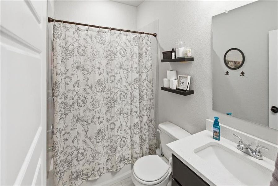 Bathroom featuring a quartz vanity, a textured wall, and shower / tub combo Bathroom featuring a quartz vanity, a textured wall, and shower / tub combo