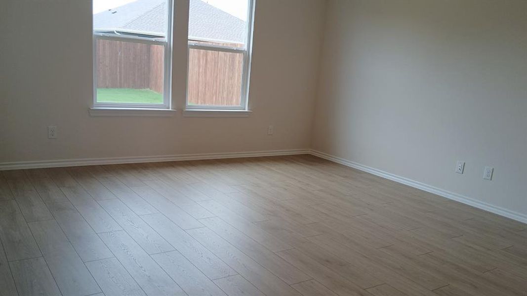 Spacious room with wood-finish flooring, light-toned walls, white baseboards, and two large windows Spacious room with wood-finish flooring, light-toned walls, white baseboards, and two large windows