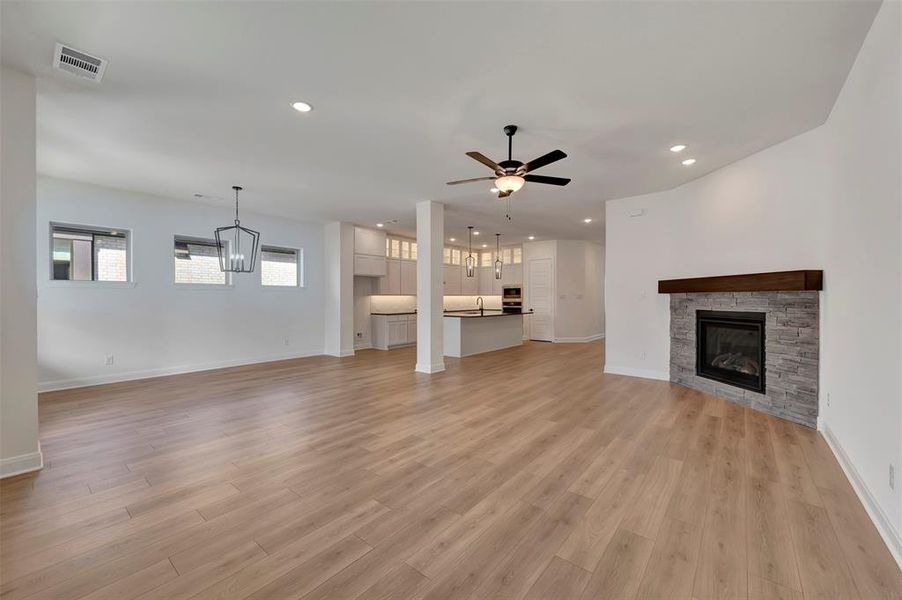 Unfurnished living room featuring a fireplace, ceiling fan, light wood finished floors, and a chandelier