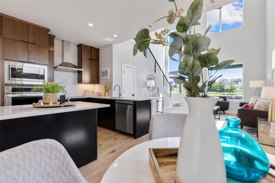 Kitchen featuring a peninsula, stainless steel appliances, backsplash, wall chimney exhaust hood, and light stone counters