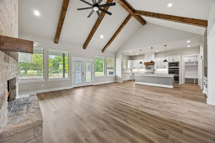 Unfurnished living room with a stone fireplace, high vaulted ceiling, light wood-style floors, recessed lighting, and french doors Unfurnished living room with a stone fireplace, high vaulted ceiling, light wood-style floors, recessed lighting, and french doors